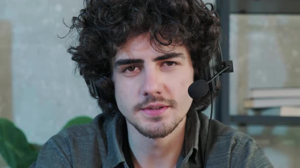 Curly Haired Young Man Looking at Camera and Talking Using a Headphones