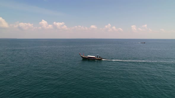 aerial drone circling a tourist on the front of a thai longtail boat in the blue andaman sea on a su
