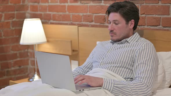 Middle Aged Man Working on Laptop in Bed