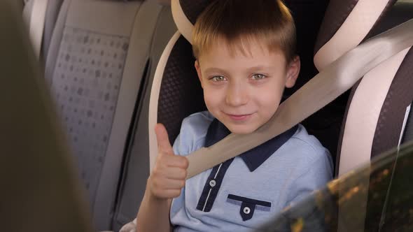 A Cheerful Child is Sitting in the Car in the Back Seat and Giving a Thumbs Up