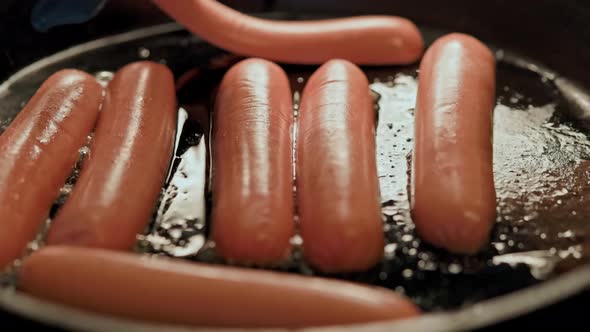 a Hand in a Blue Glove Lays Out Half of the Sausages in a Hot Frying Pan Covered with Sunflower Oil