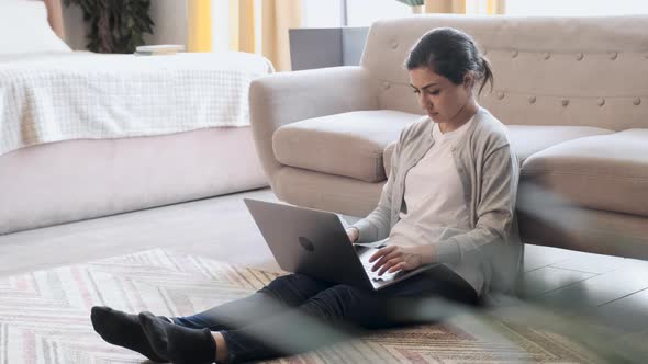 Young woman sitting on floor at home working with laptop and documents