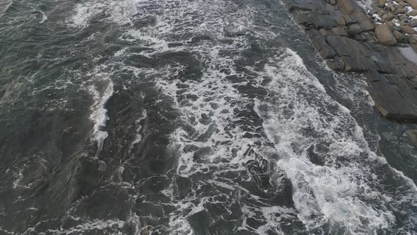 Following waves in as they wash over a rocky shoreline during winter sunrise AERIAL