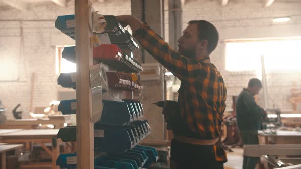 Carpentry Industry - Bearded Man Worker Walking To the Stand with Different Screws