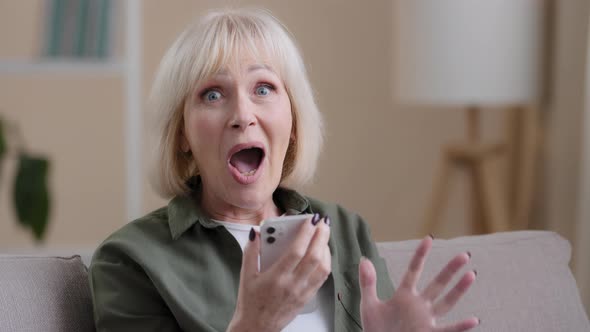 Close Up Shocked Amazed Older 50s Female at Home with Smart Phone Receive Great News Offer Win