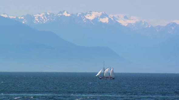 Sail boat in Victoria, BC deploys a dinghy with Olympic Mountains in the background.