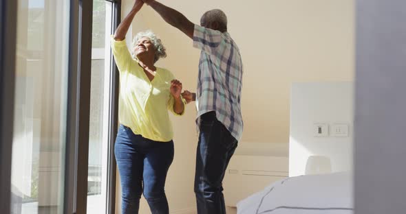 Happy senior diverse couple dancing in living room at retirement home