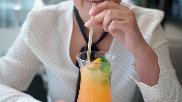 Middle Aged Caucasian Woman on Vacation Relaxed Drinks a Fruit Orange Cocktail with Mint Leaves