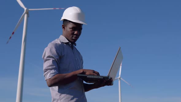 An African American Electrical Engineer is Standing Against the Backdrop of a Windmill at an Air