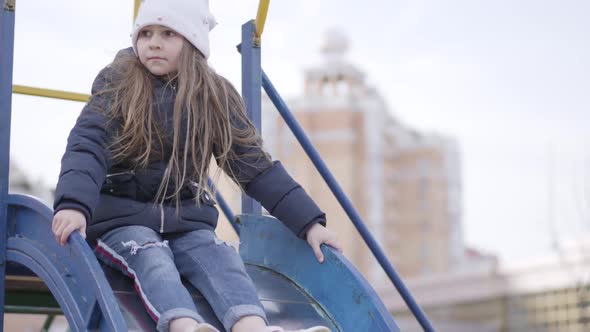 Joyful Little Girl Sliding Down the Slide on Playground. Camera Following Caucasian Child Having Fun