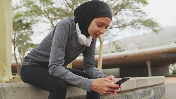 Woman in sportswear wearing hijab using her phone outside