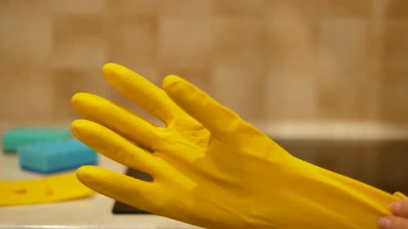 Woman Hand Puts Yellow Cleaning Glove in Front of Induction Cooktop on a Cozy Kitchen Closeup Yellow