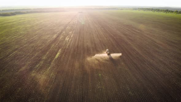 Aerial View of Farming Tractor Spraying on Field with Sprayer, Herbicides and Pesticides at Sunset