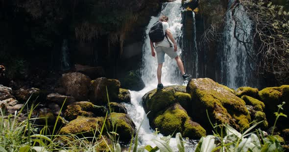 Male traveler with border collie dog walk and rise hands on waterfall on journey