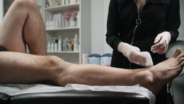 Depilation Master Removing the Excess of the Wax From the Leg of Her Male Client