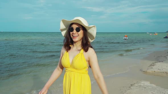 slow-motion of cheerful woman in yellow dress walking on the sea beach
