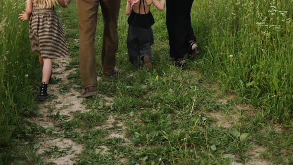 Family of Four Walks Along a Path on a Field Among Tall Green Grass