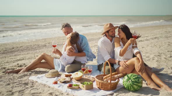 Four Millennial Friends Have Picnic on Sandy Beach at Sunny Day Next Waving Sea