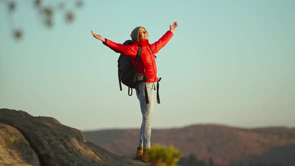 Young Inspired Woman Hiker Raises Her Hands Up Standing on Top of Mountain Above Hills Against