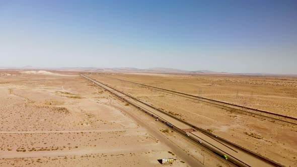 Aerial view of a long straight highway stretching through a barren dessert on a sunny day.