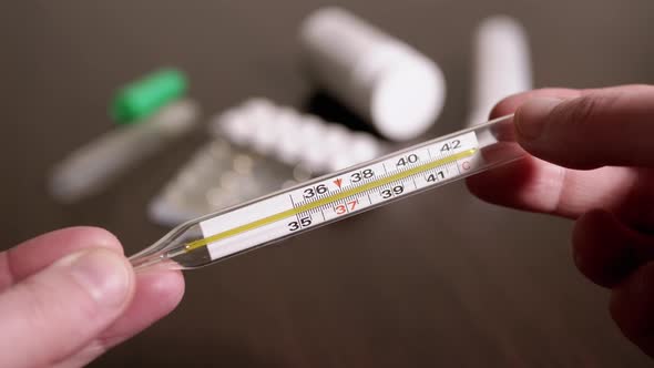 Female Hands Holding a Glass Mercury Thermometer with a High Body Temperature
