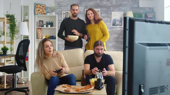 Young Couple Eating Popcorn While Their Friends Are Playing Video Games