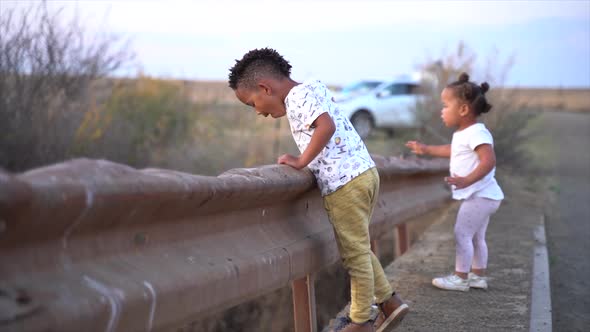 South African boy and girl on a low bridge in a winter country landscape at dusk