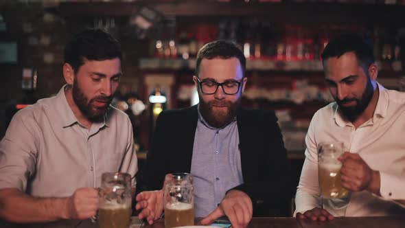 Cheerful Male Friends in Good Mood Drinking Beer and Resting After Work Day. Three Colleagues