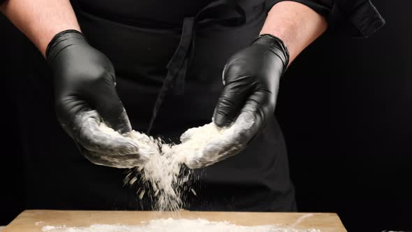 Chef in black latex gloves sprinkles white wheat flour