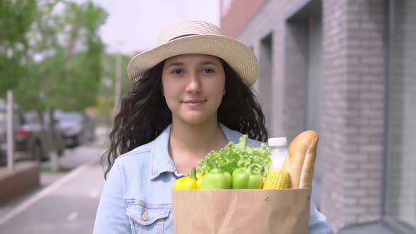 Young Beautiful Woman in a Denim Jacket and Hat Carries a Grocery Bag