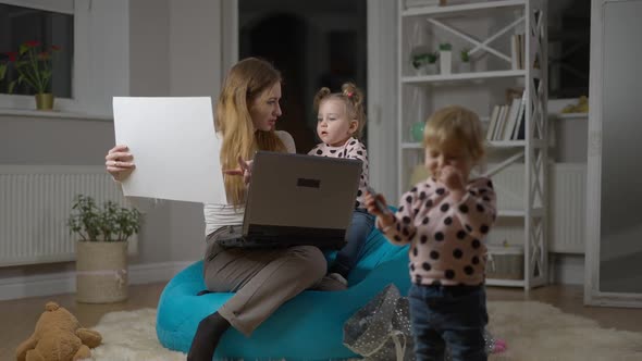 Serious Young Mother Working Online From Home Office Talking with Baby Daughter As Blurred Twin