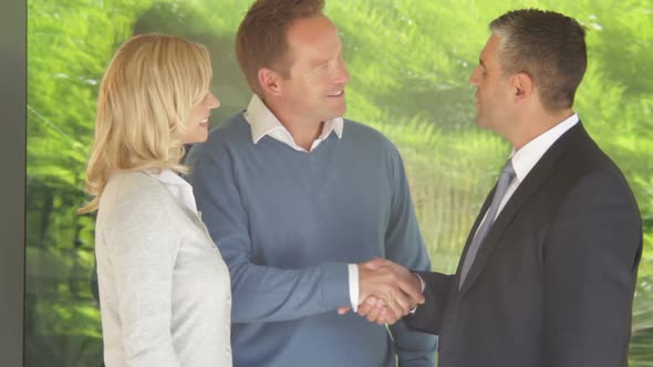 Mid Shot portrait of couple with estate agent in front of contemporary house