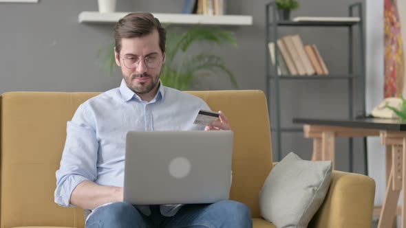 Young Man Making Online Payment on Laptop on Sofa