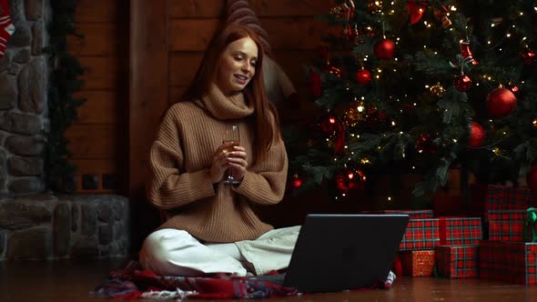 Cheerful Young Woman Talking on Laptop Sending Online Congratulations Holding Glass with Champagne.