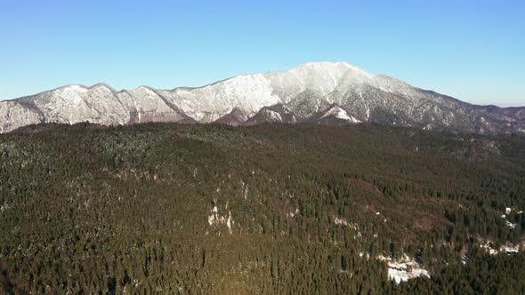 Left to right aerial tracking shot of snowy Postavarul Massif, Romania.