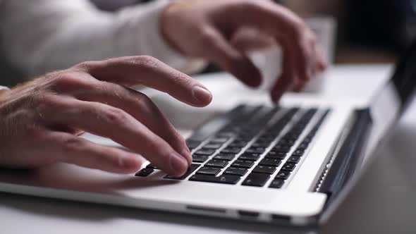 Close-up of Man Hands Typing on Laptop Keyboard at Desk in Home.