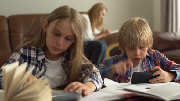 Cute Little Boy and Girl Studying at Home in the Foreground Checking Answers in the Internet