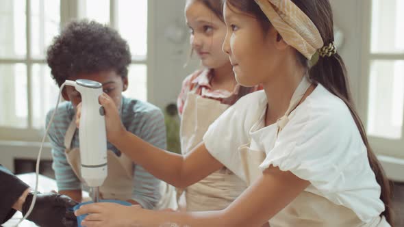 Little Asian Girl Using Hand Blender during Culinary Lesson