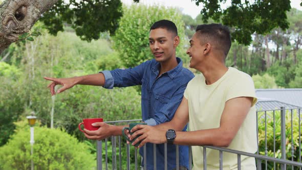 Mixed race gay male couple standing in garden drinking cups of coffee talking and laughing