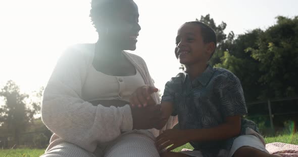 Happy african pregnant mother having tender moment with son at park