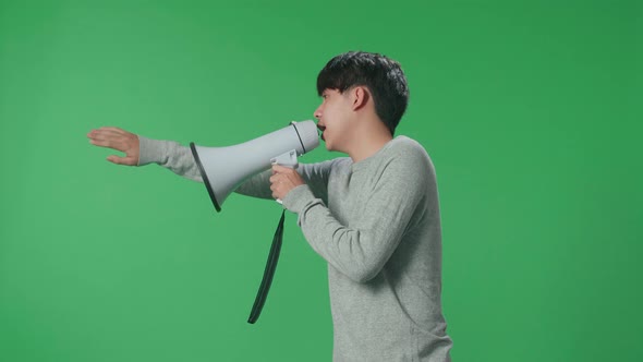 Side View Of Asian Man Speaking On Megaphone In The Green Screen Studio