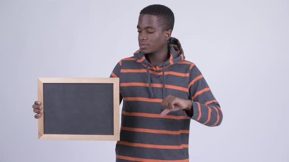 Young Stressed African Man Holding Blackboard and Giving Thumbs Down