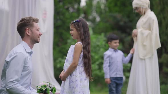 Side View of Charming Little Middle Eastern Girl Talking with Caucasian Man with Wedding Bouquet As