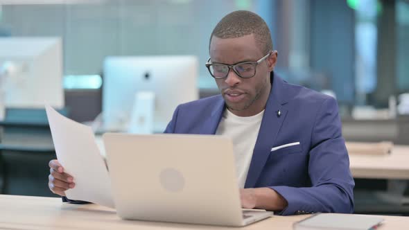 Businessman with Laptop Reading Documents in Office