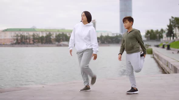 Asian Mother and Son Doing Stretching Exercise on Urban Riverside Sidewalk