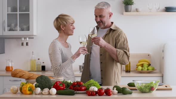 Spouses Clinking Glasses Drinking Wine Preparing Dinner Together In Kitchen