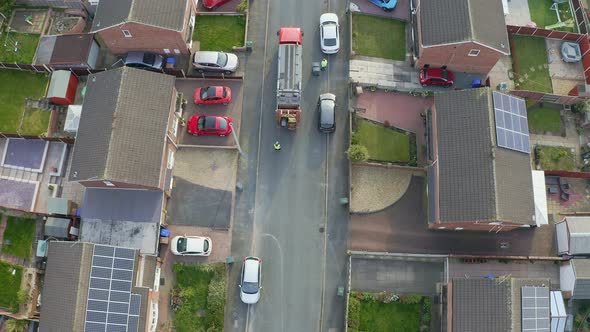 A bin lorry, refuse collection vehicle makes it way up the road as men load recycling bins into the