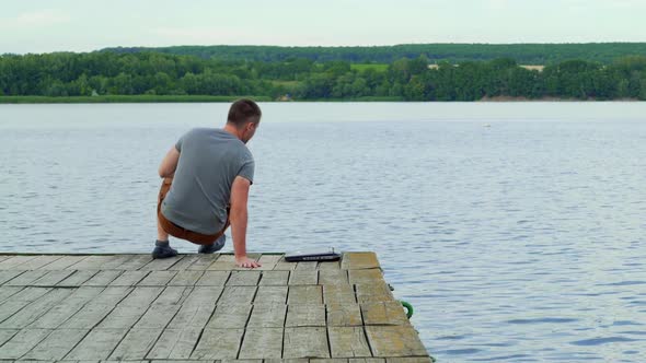 Man with his notebook is working outdoor at the lake. Old wooden pier