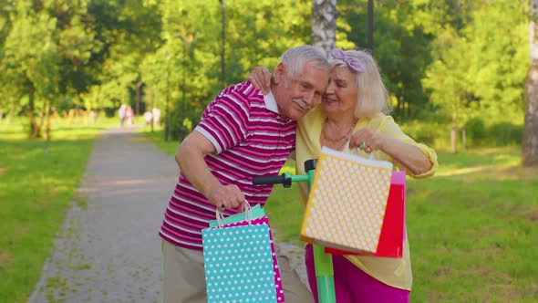 Elderly Stylish Couple Grandmother Grandfather After Shopping with Bags Using Scooter for Riding