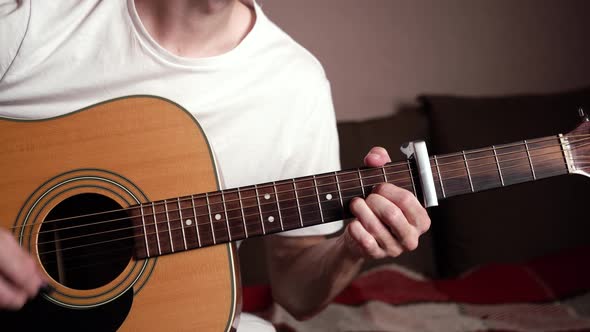 young man in white t-shirt playing acoustic guitar. cozy room